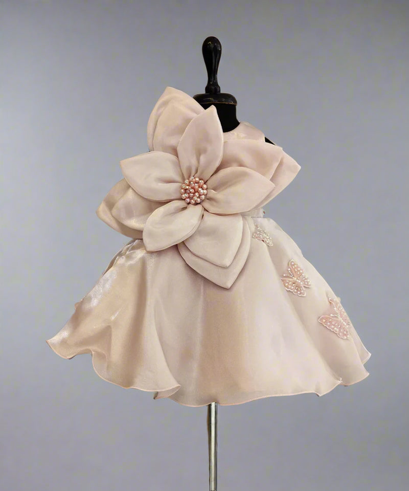 A peach-colored baby birthday frock was displayed on a mannequin, featuring a floral design and a large bow on the chest.