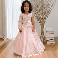 Young girl in a pink dress with a large bow standing indoors.