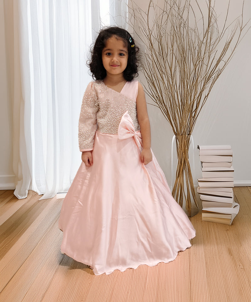 Young girl in a pink dress with a large bow standing indoors.
