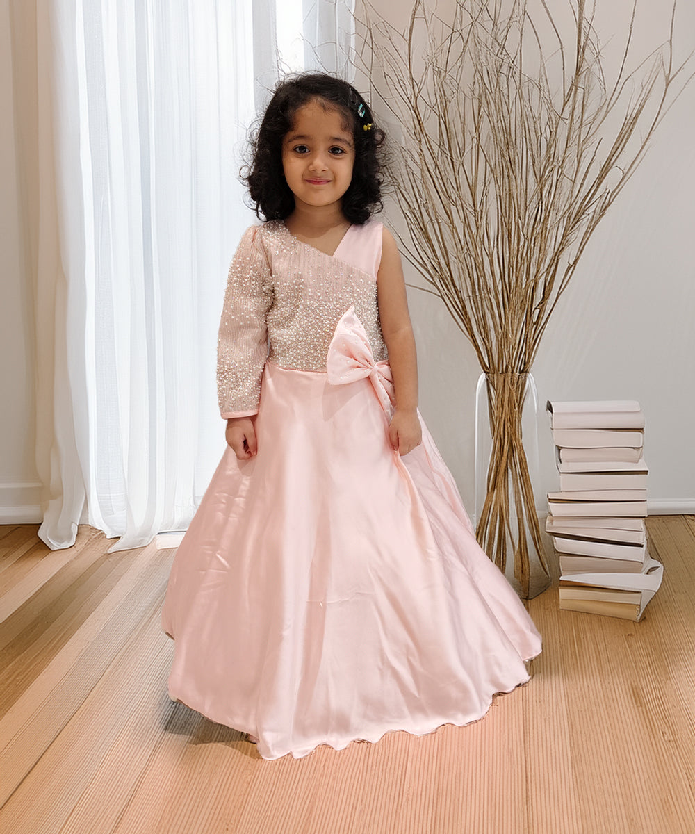 Young girl in a pink dress with a large bow standing indoors.
