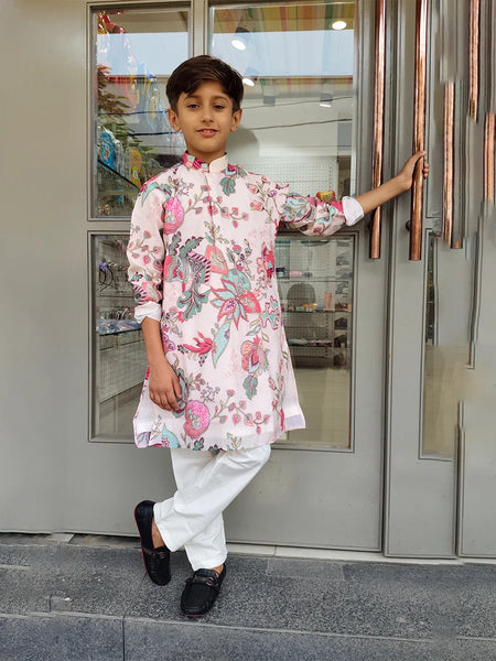 Child wearing a floral kurta with white pants standing in front of a glass door.