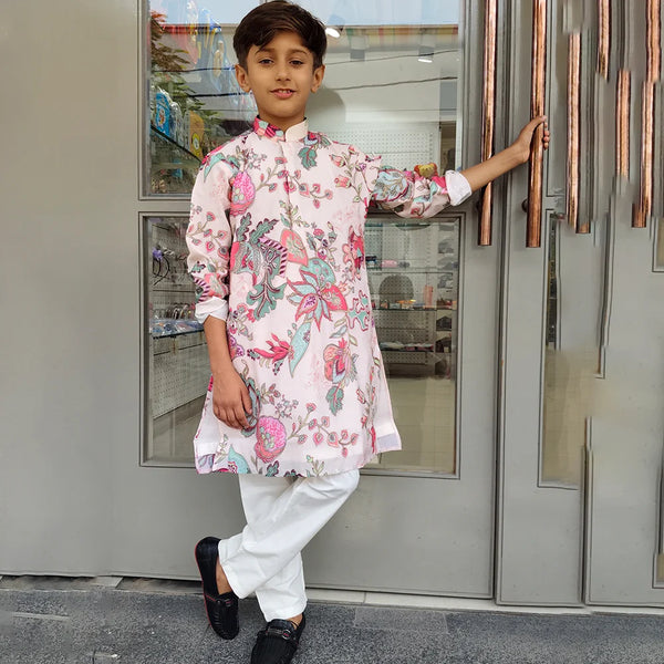 Child wearing a floral kurta with white pants standing in front of a glass door.
