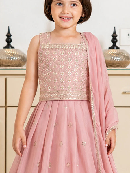 Young girl in a pink traditional outfit with floral patterns indoors.