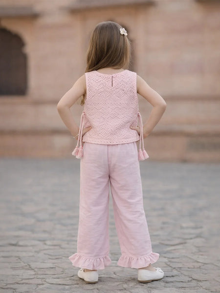 Young girl wearing a pink outfit standing on a stone pavement with a blurred architectural background.
