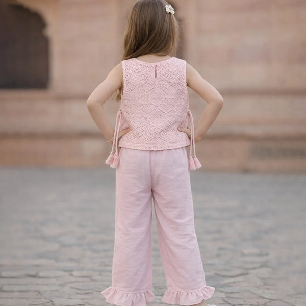 Young girl wearing a pink outfit standing on a stone pavement with a blurred architectural background.