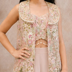 A sleeveless embellished vest with a wide decorative collar, shown on a model wearing a matching cropped top and light pink pants against a neutral beige background.