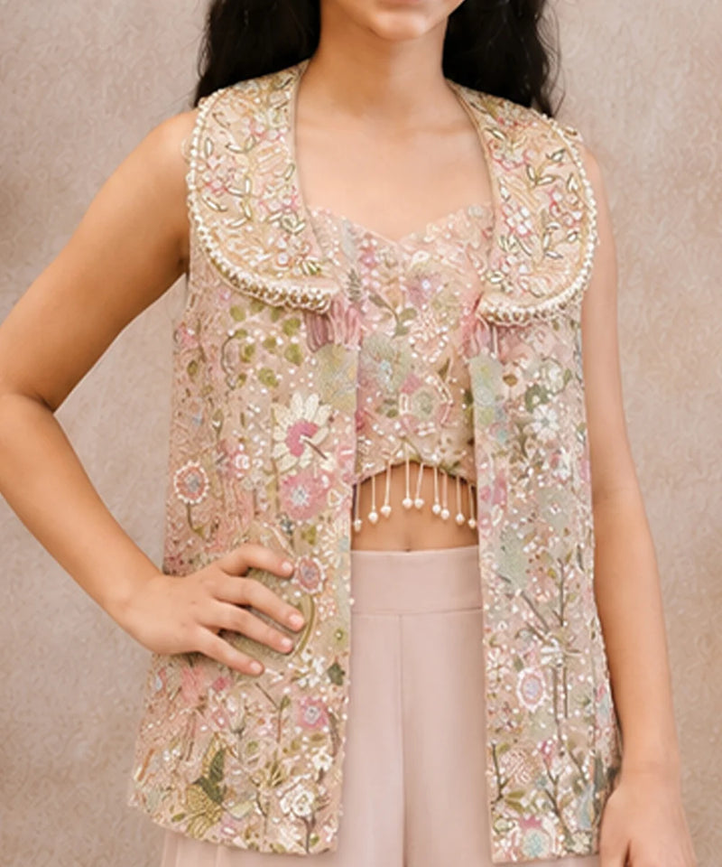 A sleeveless embellished vest with a wide decorative collar, shown on a model wearing a matching cropped top and light pink pants against a neutral beige background.