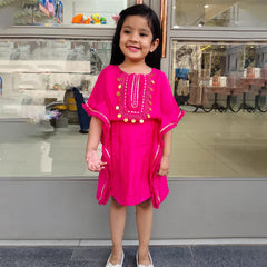 A girl wearing a pink kaftan style dress with embellishments, standing in front of a store display.