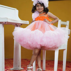 It's a pink and orange Colored frock that comes with a hook closure and a fabric belt to be tied at the back. It features matching hair accessory, frills on one shoulder, pleated and pearl detailing on the yoke.