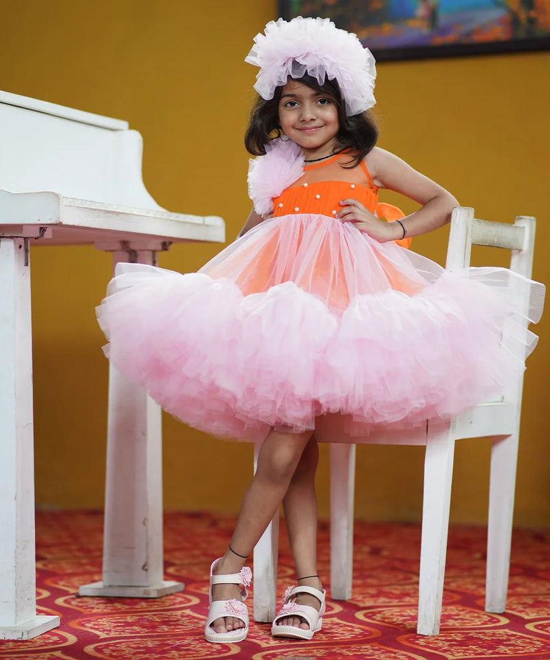 It's a pink and orange Colored frock that comes with a hook closure and a fabric belt to be tied at the back. It features matching hair accessory, frills on one shoulder, pleated and pearl detailing on the yoke.