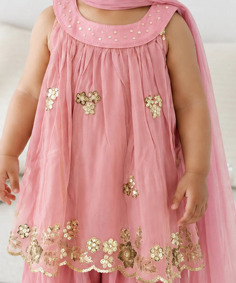 A pink sleeveless dress with gold floral embroidery and sequins, worn by a child. The dress features a scalloped hem with gold floral applique and a matching pink dupatta draped over the shoulders.