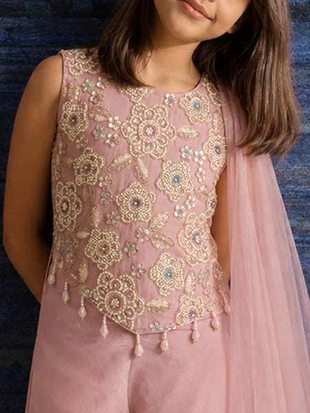 A child wearing a sleeveless dusty pink traditional outfit with intricate gold floral embroidery and beadwork, paired with a sheer pink dupatta, set against a dark blue textured background.