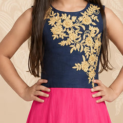 A sleeveless navy blue dress with intricate gold floral embroidery on the bodice, worn by a child with a bright pink skirt, set against a beige patterned backdrop.
