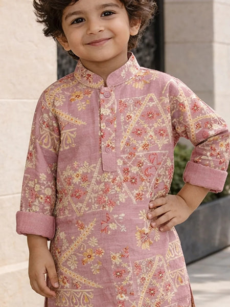 Child wearing a pink traditional outfit with floral patterns standing outdoors.