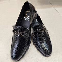 Pair of black loafers with a chain detail on a light background
