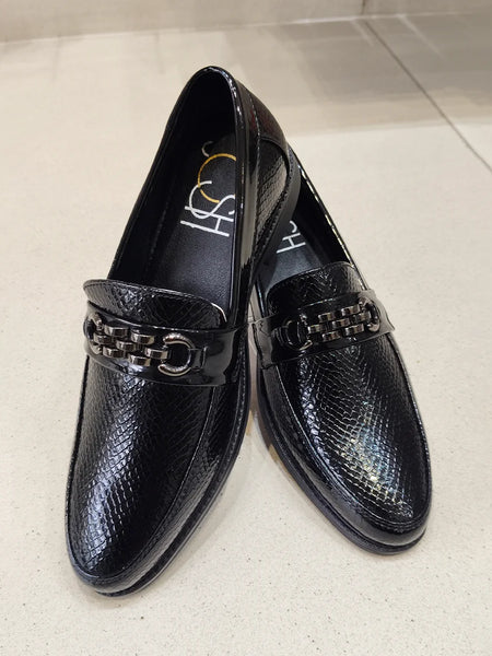 Pair of black loafers with a chain detail on a light background