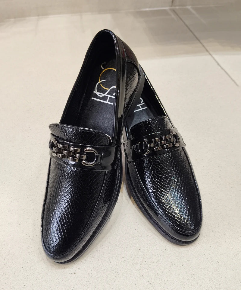 Pair of black loafers with a chain detail on a light background
