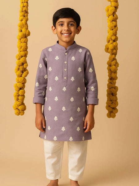 Child wearing a purple kurta with white patterns and white pants on a beige background