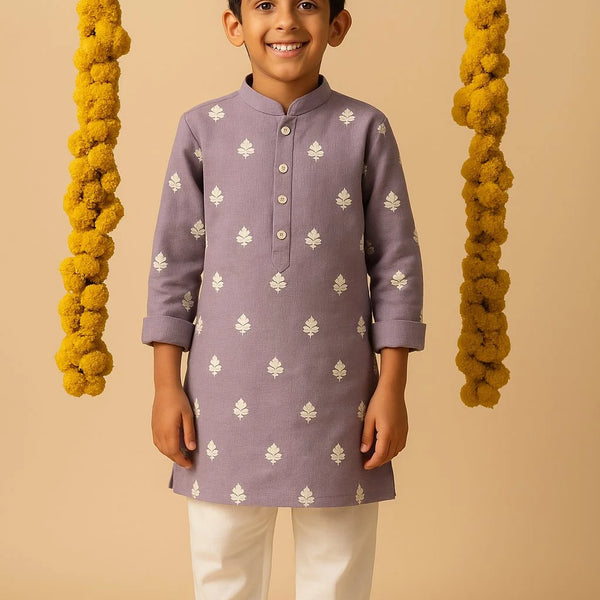 Child wearing a purple kurta with white patterns and white pants on a beige background