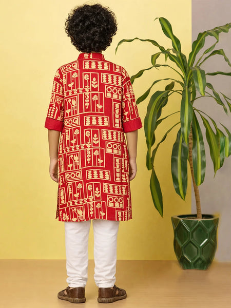 Person wearing a red and white patterned kurta with white pants, standing against a yellow wall with a plant.