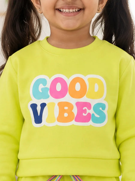 A close-up of a smiling child wearing a bright lime green sweatshirt with the words 'GOOD VIBES' printed across the chest in large, colorful bubble letters.