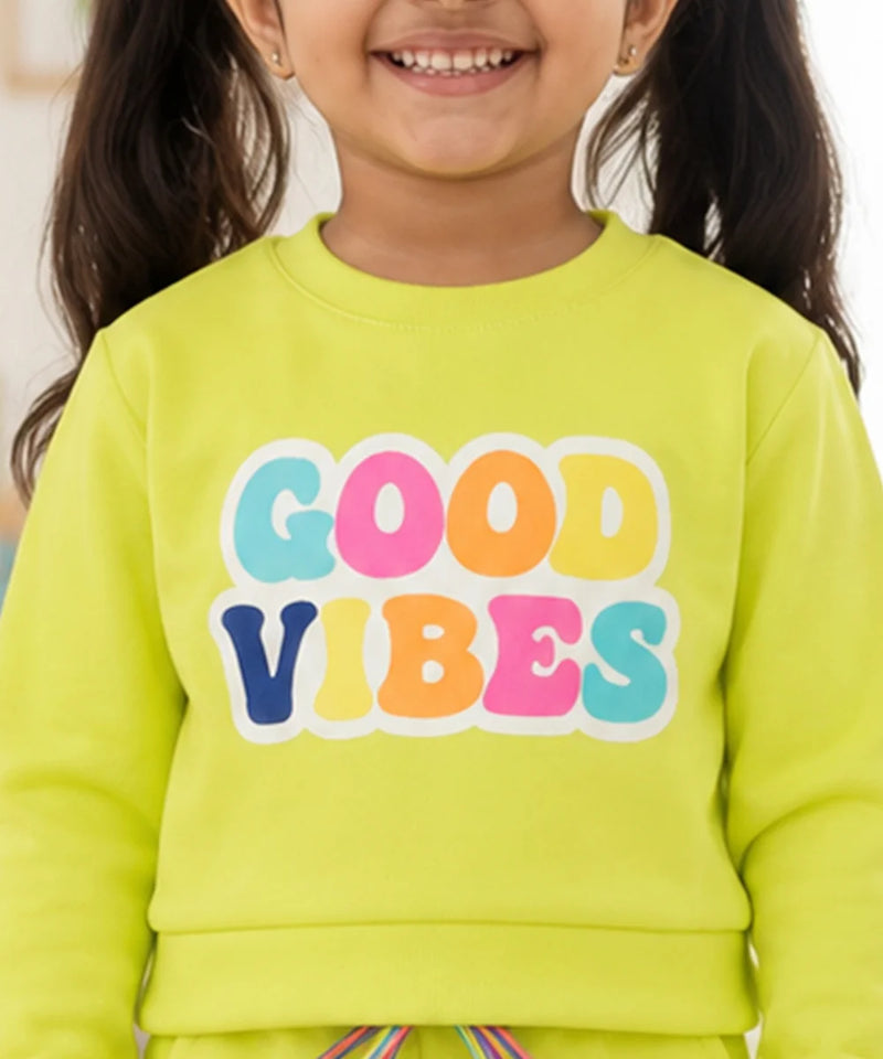 A close-up of a smiling child wearing a bright lime green sweatshirt with the words 'GOOD VIBES' printed across the chest in large, colorful bubble letters.