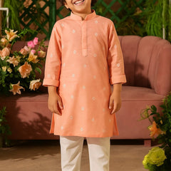 Child wearing an orange kurta with white pants standing in a decorated room.