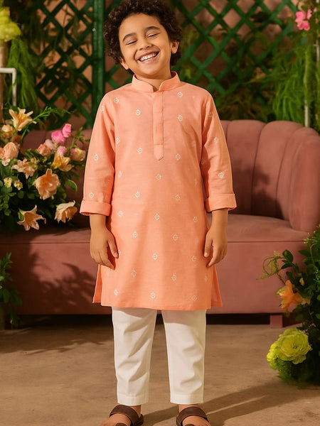 Child wearing an orange kurta with white pants standing in a decorated room.