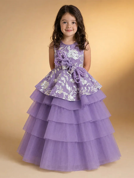 A young girl with dark curly hair wearing a lavender purple formal party dress with white floral embroidery and a tiered tulle skirt, standing against a warm beige studio background.