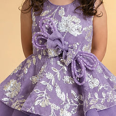 A sleeveless purple dress with a silver floral pattern, featuring a large purple bow at the waist, worn by a child against a solid beige background.