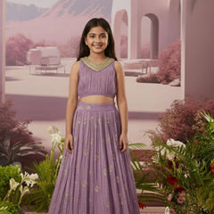 Young girl in a purple traditional outfit standing in a decorative setting with flowers and arches.