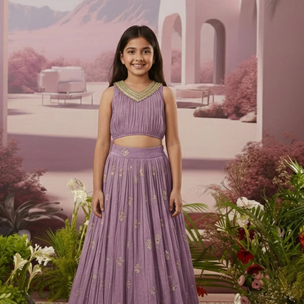 Young girl in a purple traditional outfit standing in a decorative setting with flowers and arches.