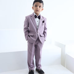A boy wearing a purple tuxedo with a peak lapel collar, full sleeves, and a matching bow tie, standing against a white background.