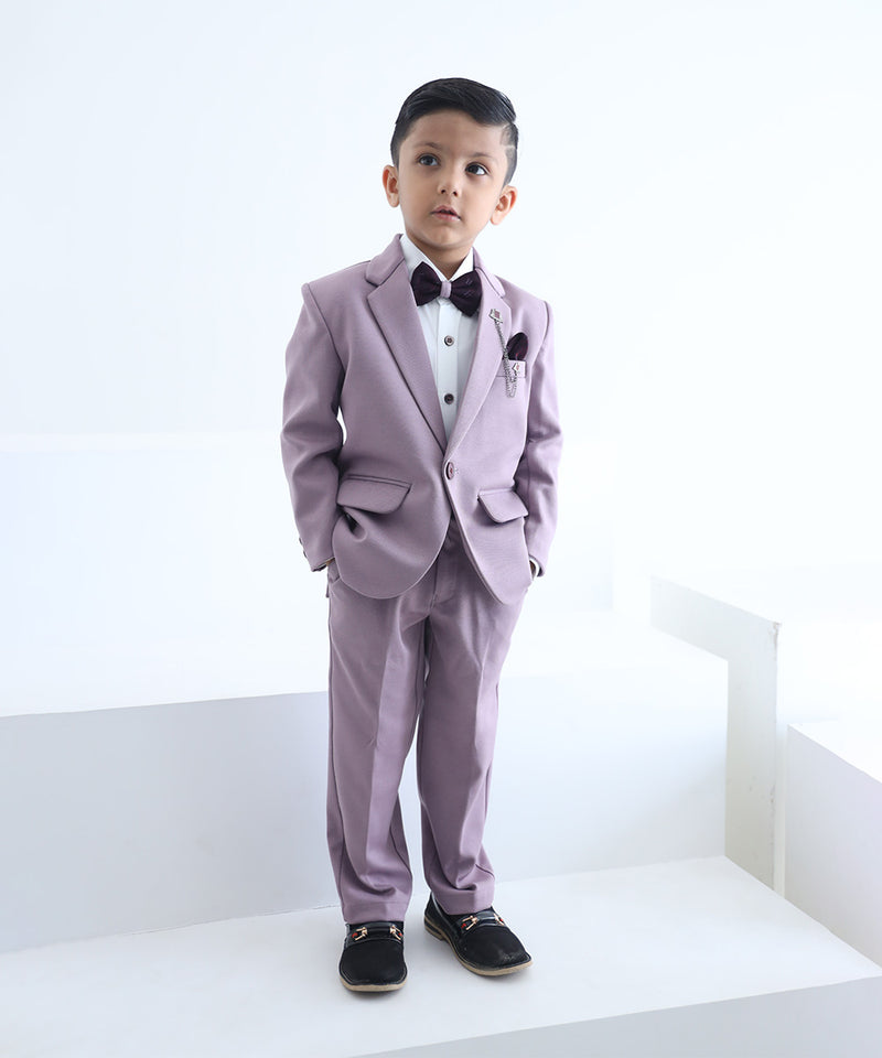 A boy wearing a purple tuxedo with a peak lapel collar, full sleeves, and a matching bow tie, standing against a white background.