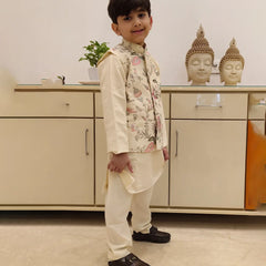 It is a side view of boy wearing a cream color kurta pajama with an embroidery jacket