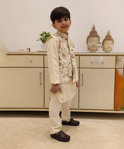 It is a side view of boy wearing a cream color kurta pajama with an embroidery jacket