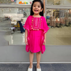 Young girl in a bright pink dress standing in front of a store window.