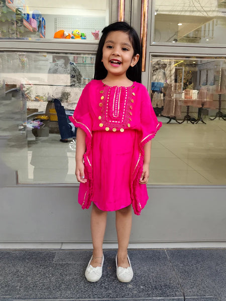 Young girl in a bright pink dress standing in front of a store window.