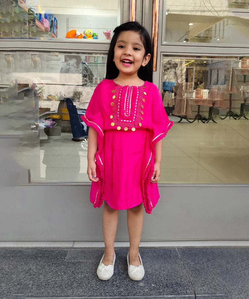 Young girl in a bright pink dress standing in front of a store window.