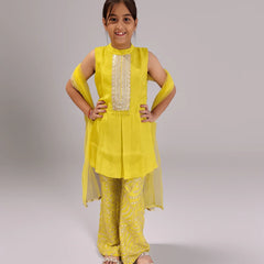 Young girl wearing a yellow sharara traditional outfit with a plain background