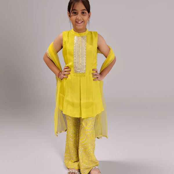 Young girl wearing a yellow sharara traditional outfit with a plain background