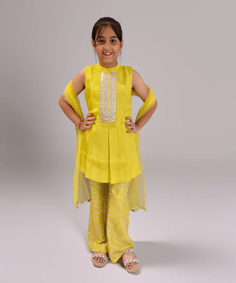 Young girl wearing a yellow sharara traditional outfit with a plain background