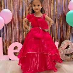 A young girl in a red party wear gown with a bow at the waist, standing in front of a decorative backdrop with balloons and the letters 'L O V E'.