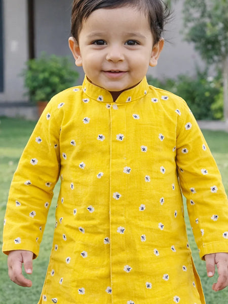 Child wearing a yellow traditional outfit with floral patterns outdoors.
