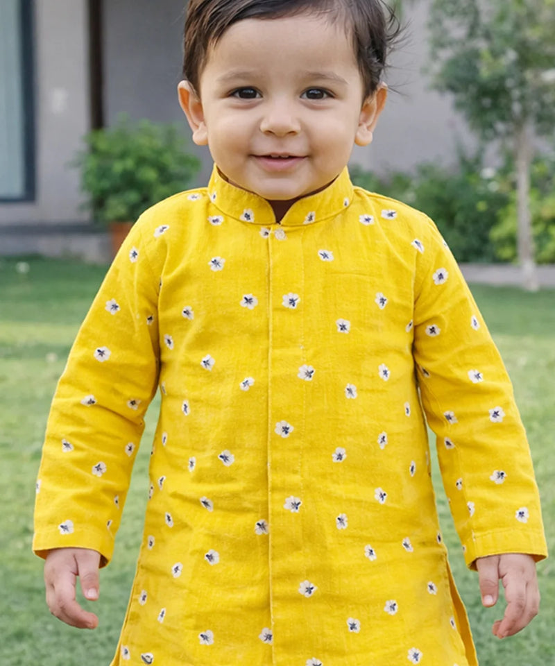 Child wearing a yellow traditional outfit with floral patterns outdoors.