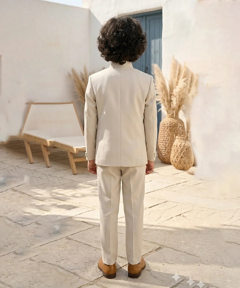 Person wearing a beige suit standing in a sunlit outdoor setting with decorative plants and a chair.