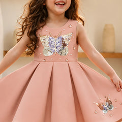 Young girl wearing a pink dress with butterfly embellishments indoors.