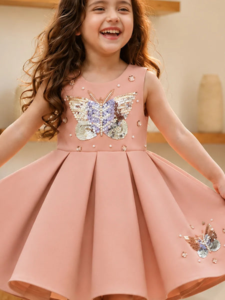 Young girl wearing a pink dress with butterfly embellishments indoors.