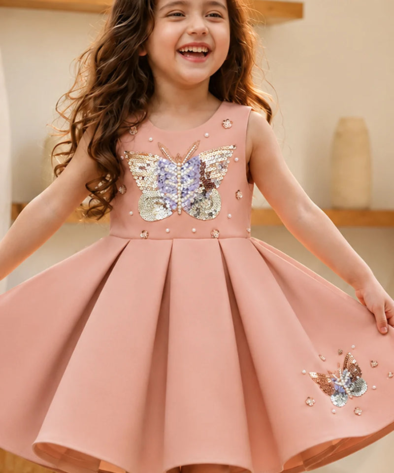 Young girl wearing a pink dress with butterfly embellishments indoors.