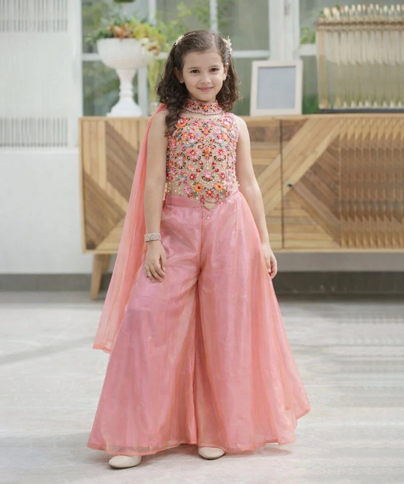 Young girl in a pink traditional outfit with floral top in a bright room.